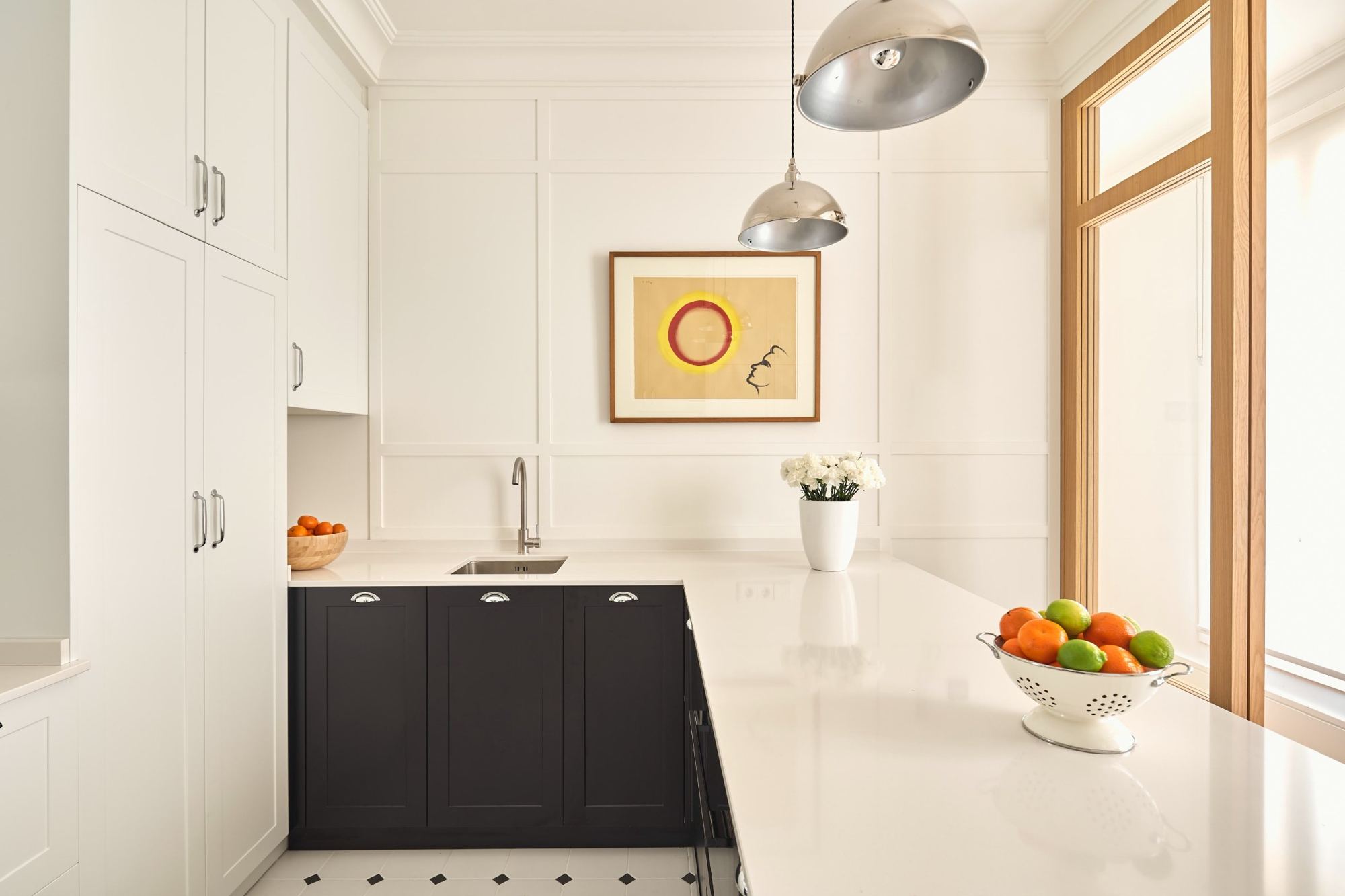 Kitchen peninsula in white stone with navy cabinetry and chrome pendants
