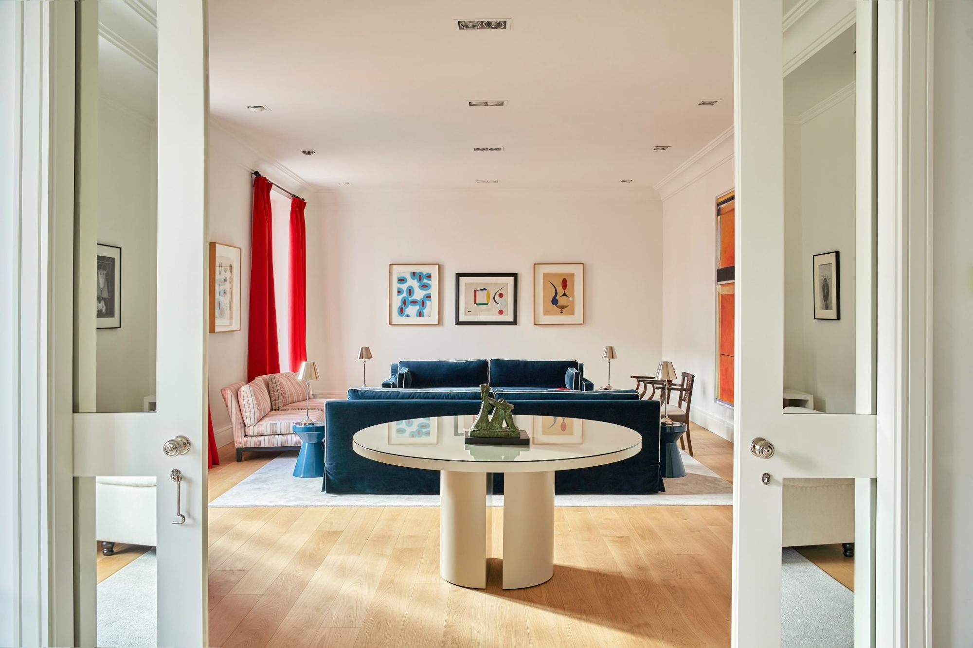 The living room seen through glazed double doors, round table and navy sofas