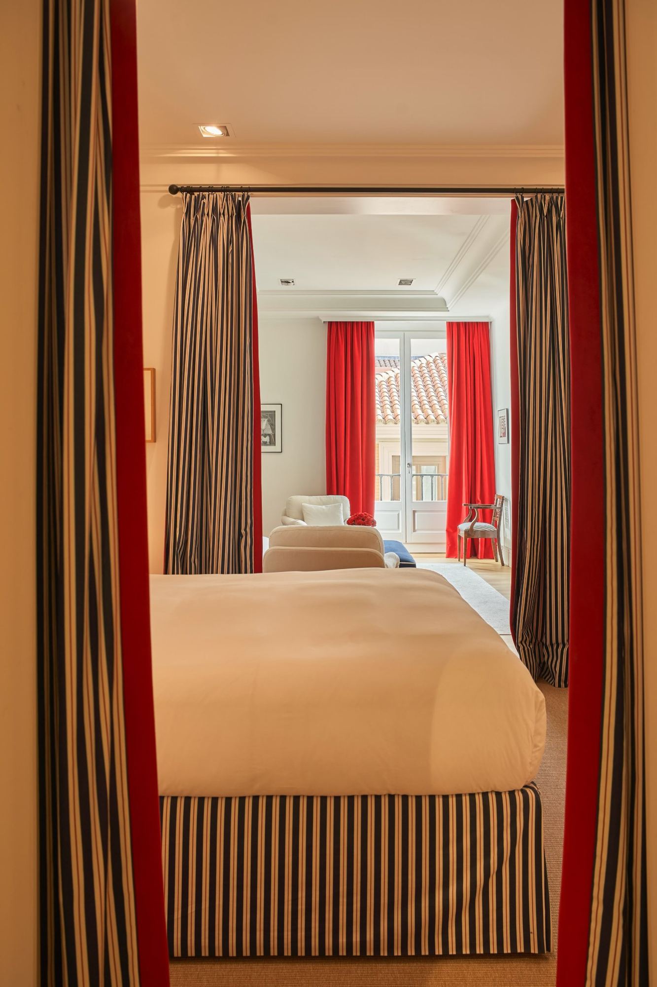 Master bed with striped skirt between red and striped curtains