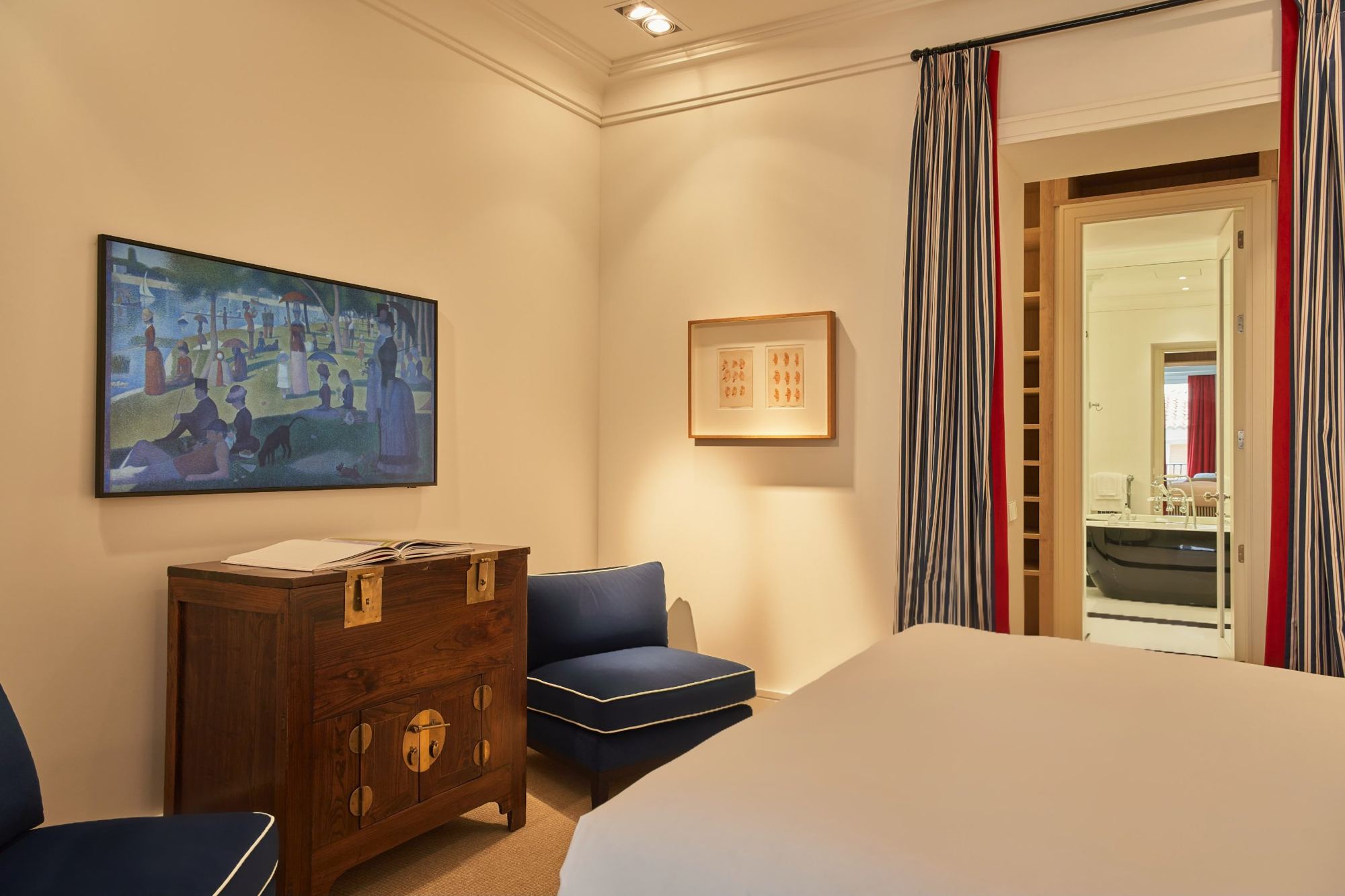 Master bedroom with navy armchairs, antique chest and a view through to the bath