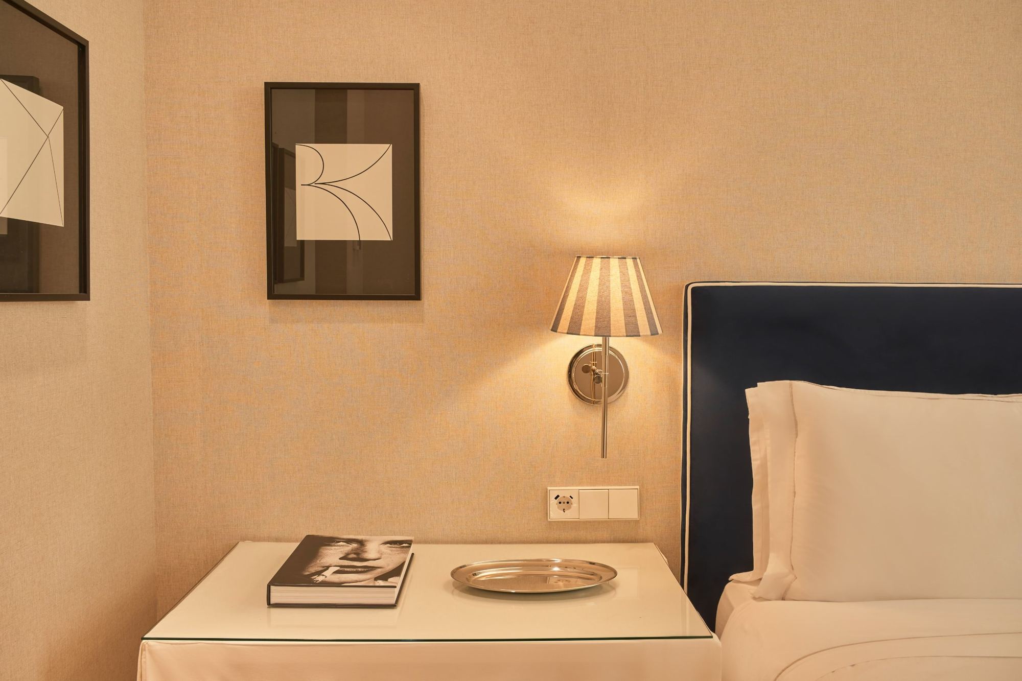 Suite bedside: striped sconce, black-framed print and navy headboard